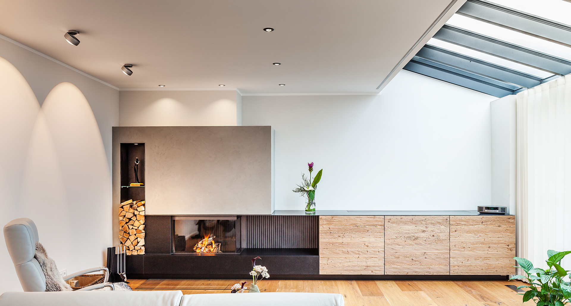 Ein Modern eingerichtetes Wohnzimmer mit Deckenfenster, Holz-Laminat und eingebauten Kamin.